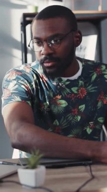 Canlı çiçekli gömlekli kendini işine adamış profesyonel bir adam masasının yanında bir bitkiyle birlikte çalışıyor.