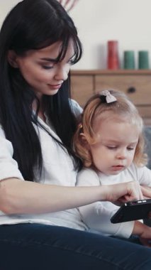 İlgili bir anne, modern ebeveynlik tekniklerini vurgulayan akıllı telefonu araştıran küçük çocuğuyla etkileşim halindedir.