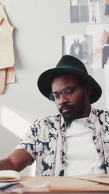 Şık giyinmiş bir moda tasarımcısı, eskizlerle çevrili yaratıcı bir çevrede çalışmaya odaklanmış..