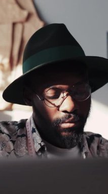 Şık gözlüklü ve şık şapkalı odaklanmış bir insan modern bir çalışma alanında tasarım yapmakla meşgul.