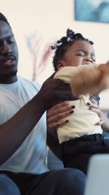 Genç bir çocuk mutlu bir şekilde renkli bir oyuncakla oynuyor ve bir ebeveynin kucağında rahatça oturuyor.