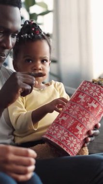 Neşeli bir sahne şefkatli bir baba ve çocuğun birlikte sevgi dolu bir hediye paketleme anını paylaştığını gösteriyor.