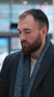 Şık bir atkı ve bakımlı bir sakalı olan genç bir adam modern bir ortamda güzel bir şekilde yakalanır.