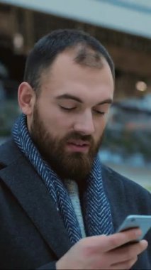 Bir adam, etrafını çevreleyen canlı ve renkli bir arkaplan arasında akıllı telefonuyla derinden ilgilenir.