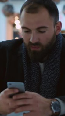 Sakallı genç bir adam akıllı telefonuna dalmış sıcak bir ortamda, sosyal medya ve yaşam tarzı temaları için mükemmel..