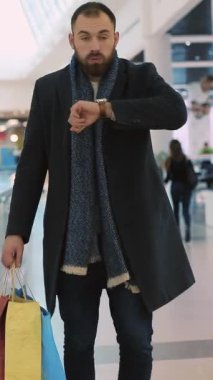 Bir adam hareketli alışveriş merkezlerinde geziyor, canlı alışveriş torbalarıyla, modern bir hava ve şık bir tat sergiliyor