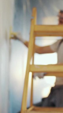 NEW YORK - 5 Nisan 2017: Merdivendeki bir işçi çizim malasını kullanırken, sakallı iş arkadaşı duvarı boyamak için boya silindiri kullanıyor. Sıkı çalışma, saatlik ödeme, profesyonel ekip. Yavaş çekim, kamera dengeleyici çekim