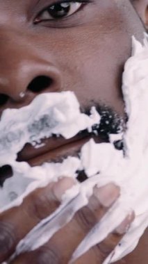 Bir adam, titiz ve titiz cilt bakımı rutinini göstermek için, yüzüne dikkatlice sakinleştirici krem sürer.