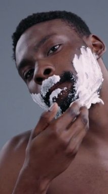 Bir adam dikkatlice yüzüne tıraş kremi sürüyor günlük bakım rutinini ve cilt bakımını sergiliyor.