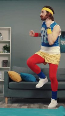 Konforlu bir oturma odasında yoga yapan, zıplayan ve paspasın üzerinde dans eden bir adamın canlı videosu.