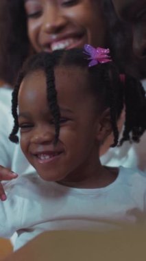 Saçı örgülü bir kız ve neşeli bir anı paylaşan bir kadının yürek ısıtan bir sahnesi. Mor çiçekli kız, neşeli bir şekilde gülüyor, güçlü bağlarını gösteriyor.