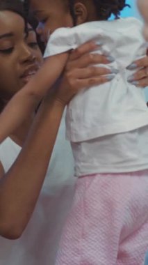 Bir kadın, sevgi dolu kollarında küçük tatlı bir kızı nazikçe kucağında tutuyor. Bu samimi anda sıcaklık ve şefkat saçıyor.