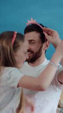 Bir adam sevgiyle küçük bir kızın kafasına pembe bir saç bandı takar ve bağlarını gösterir. O da bir tane takıyor, onu neşeli bir dansa götürüyor.