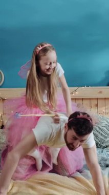 Bu iç açıcı videoda, bir adam ve küçük bir kız, çocukluk masumiyeti ve mutluluğunu gösteren rahat bir yatakta neşeyle oynuyorlar.