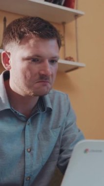 Mavi gömlekli bir adam bir masada oturuyor, dizüstü bilgisayarına odaklanıyor, ciddi ama tesadüfi bir atmosferi yansıtıyor, teknolojinin kararlardaki önemini vurguluyor.