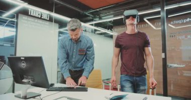 Bu ilgi çekici videoda, bir adam bilgisayarına odaklanmış bir arkadaşının yanında sanal gerçekliği keşfediyor, sanal ve gerçek görevler arasındaki farkı vurguluyor.