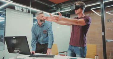 VR kulaklıklı bir adam dijital dünyaya dalarken, yakınındaki başka bir adam büyüleniyor. Sezgilerini, gerçekliği ve sanal alemi birbirine bağlayıp VR 'ların artan etkisini vurguluyor.