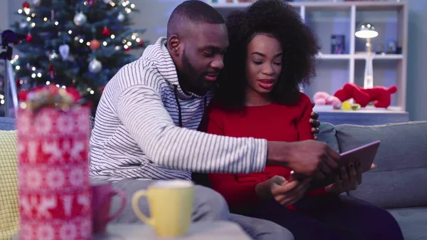 NEW YORK - 13 Aralık, 2017. Kırmızı kazaklı güzel kıvırcık kız kanepede oturuyor ve arka planda harika bir ağaç var. Tablet kullanan kız. Sarılmak..