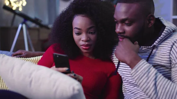 İki çekici genç insan akıllı telefona dikkatle bakıyor. Aşık çift cep telefonu kullanıyor. Yakın plan. Noel atmosferi.