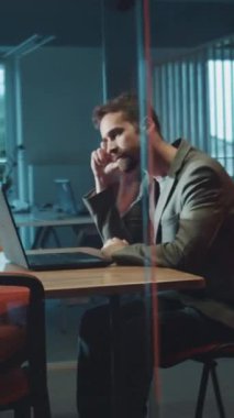 Takım elbiseli profesyonel bir adam şık bir masada dizüstü bilgisayarıyla meşgul oluyor ve modern bir çalışma alanında odaklanmış bir atmosfer yaratıyor.