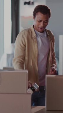 Afro-Amerikalı genç erkek arkadaşı karton kutuları yapıştırıcı bant kullanarak paketlemesine yardım ediyor. Taşınan ev.