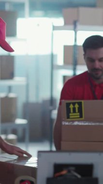 Postanede işbirliği yapan, kırmızı üniformalı, beyaz erkek işçiler. Meslektaşı Karton Kutuları Tararken Bir Adam Teslimat Paketleri Taşıyor.