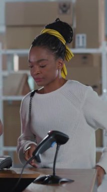 Paket almak için postaneye gelen modern, genç Afrikalı bir kadın. Birkaç genç ve olgun posta işçisi müşterilerine karton kutu teslim ediyor..