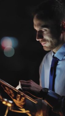 Bir adam dikkatle tabletine bakıyor loş bir ortamda, modern teknolojinin güzelliğini gösteriyor.