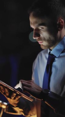 Profesyonel bir adam tabletine odaklanmış, düşüncelere dalmış ve yumuşak ortam ışıklarıyla aydınlanmış.