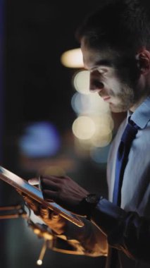 Kendini işine adamış bir profesyonel, loş bir ofis ortamında, dikkatle odaklanmış bir tablet üzerinde çalışır.