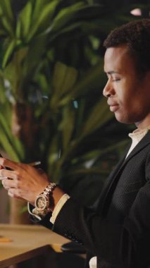 Dalgın bir adam şık bir masada tek başına, yemyeşil bir ortamda, düşünceli bir şekilde serinletici bir içki tutuyor.