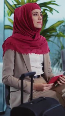 Kırmızı tesettürlü bir kadın yanında açık bir bavulla bir sandalyeye oturur. Telefonuna bakarken düşüncelere dalmış yaklaşan yolculuğunu düşünüyor.