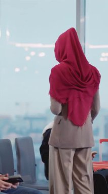 Bu video havaalanındaki tesettürlü bir kadını gösteriyor. Seyahat belgelerine yansıyor ve direnç ve kültürel kimliği simgeleyen bir kitaba gömülüyor.