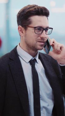 Takım elbiseli bir profesyonel cep telefonuyla konuşuyor, özgüven ve kararlılık gösteriyor. Video onun odaklanma ve iletişimini vurguluyor.
