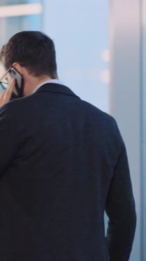 Takım elbiseli bir iş adamı telefonda kararlılık ve güven gösteriyor. Kollarını kavuşturmuş, geniş bir pencerenin kenarına bakıyor. Işık hırsını vurguluyor.