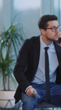 Modern bir ofiste, siyah ceketli bir adam acil bir çağrı yapar. Takım elbiseli bir başkası ise düşünceli bir şekilde oturur ve sakin bir atmosferin ortasında notlar tutar.