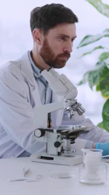 Tıp laboratuarının iç kısımlarında aşı geliştirme için mikroskop kullanan genç Kafkas doktor terapisti..