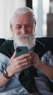 Uzun sakallı başarılı bir yetişkin emeklisi cep telefonu uygulaması kullanıyor sosyal medya mesajlaşma sevindirici teknolojisi. Ev dairesi.