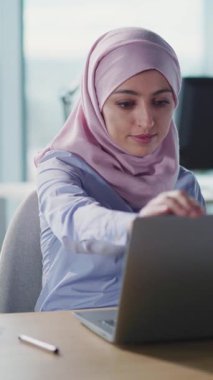 Çağdaş bir ofis ortamında tesettürlü genç bir kadın, işi için aktif olarak bir tablet kullanıyor.