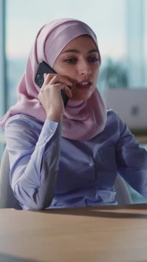 Şık tesettürlü kararlı bir kadın çalışırken akıllı telefonuyla anlamlı bir konuşma yapıyor.