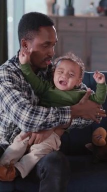 Afrikalı Amerikalı genç baba, küçük oğluyla oturma odasında oynuyor. Kanepede birlikte dinleniyorlar. Aileler. Sevgi dolu anlar. Çocukluk.