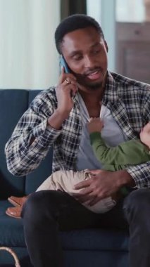 Meşgul Afrikalı Amerikalı genç baba. Ağlayan bebeği sakinleştiriyor ve telefonda konuşuyor. Serbest çalışıyor..