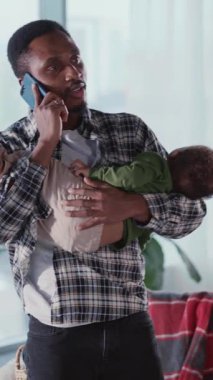 Afrikalı genç, yakışıklı işadamı babası küçük oğlunu elinde tutuyor ve iş arkadaşıyla cep telefonu konuşmaları yapıyor. Serbest çalışan biri. Bebek bakıcısı. - Evet. Babalık.