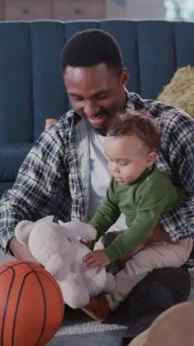 Sevecen, genç, mutlu bir baba kucağında küçük bir oğlan çocuğu oyuncaklarla oynuyor hafta sonunu evde oturma odasında geçiriyor..