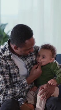 Afrikalı yakışıklı, şefkatli bir baba, ağlayan oğluyla konuşuyor. Oturma odasında kanepede oturuyor. Dairenin içinde. Aileler.