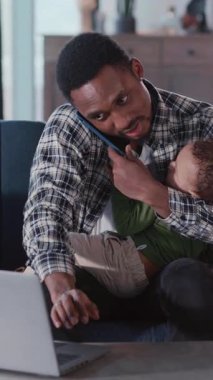 Yoğun bir yaşam tarzı. Babalık. Tecrit sırasında Afrikalı genç bir baba küçük oğluna bakıcılık yapıyor ve evden uzakta cep telefonuyla konuşuyor..