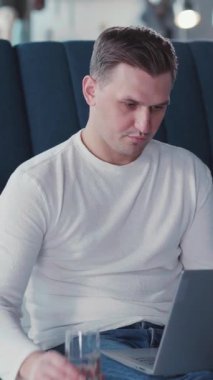 Uzak bir iş için dizüstü bilgisayar kullanan yakışıklı, genç bir yetişkin. İnternet 'te haber klavyesinde kanepeye yaslanarak vakit geçiriyor..