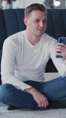 Genç yakışıklı milenyum adamı internet video konferansı için akıllı telefonu kullanıyor. Oturma odasındaki webcam ekranında konuşma ve görüntüleme yapıyor..