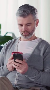 Mutlu Kafkasyalı yakışıklı yetişkin milenyumu evde boş zamanlarını cep telefonuyla çay içerek geçiriyor..