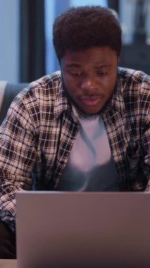 Genç bir adam dizüstü bilgisayarıyla derinden meşgul, konsantrasyonunu gösteriyor ve modern çalışma hayatını resmediyor.